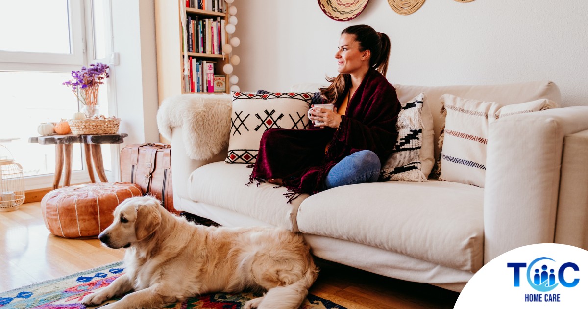 A woman relaxes with her dog while sipping on tea, representing how self-care can combat caregiver stress.