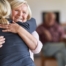 An older woman smiles as a younger woman visits her and hugs her, showing the effect that acts of kindness can have on senior loved ones.