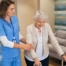 A professional caregiver helps an older client with a walker get around.