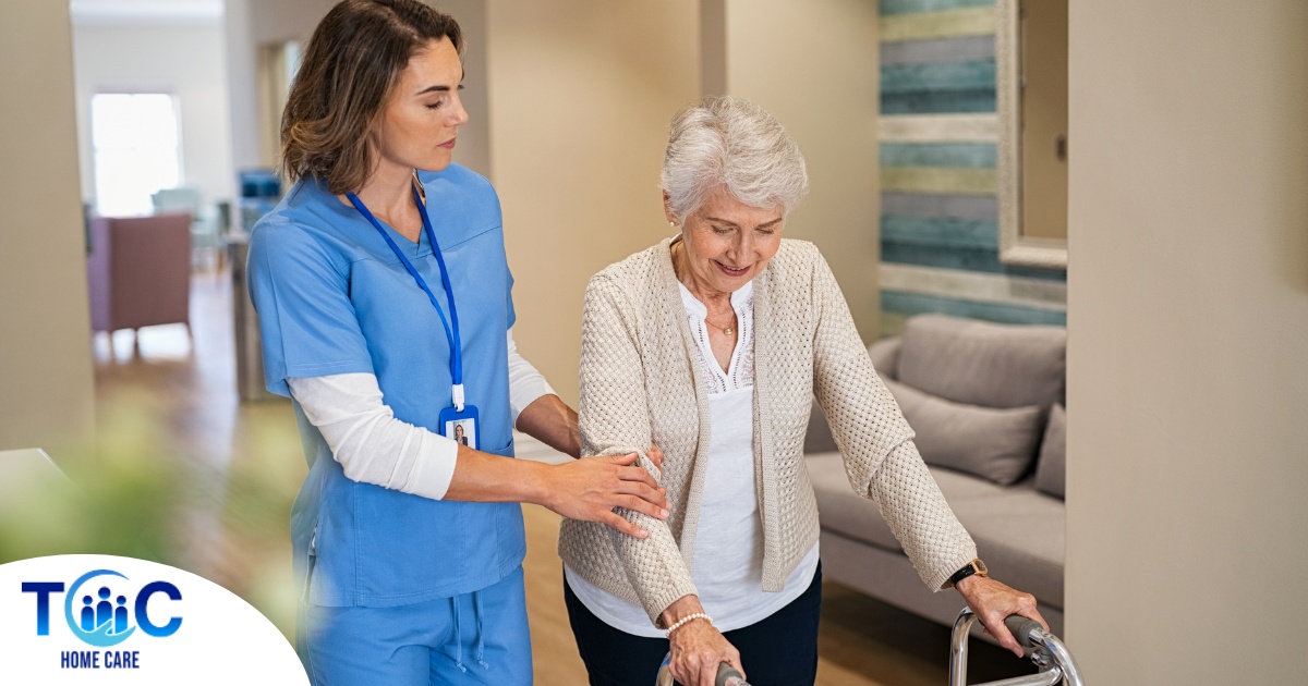 A professional caregiver helps an older client with a walker get around.