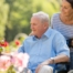 A caregiver brings an older adult with a wheelchair to see some flowers representing how professional caregivers can make outdoor activities accessible.